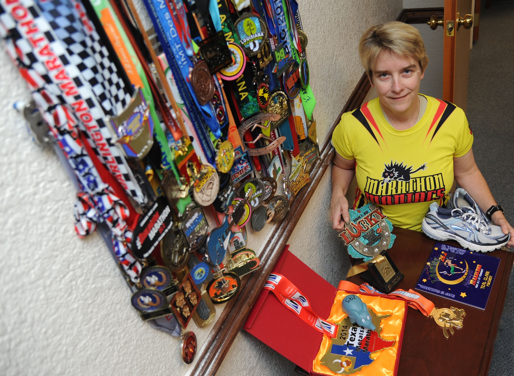 Lt. Col. Teal Clark, 2nd Air Force, takes a photo next to an assortment of marathon medals that she has on display in her office Feb. 25, 2014, at  2nd Air Force headquarters, Keesler Air Force Base, Miss.  Teal has participated in more than 50 marathons since 2010 with 34 of them completed in 2013. (U.S. Air Force photo by Kemberly Groue)