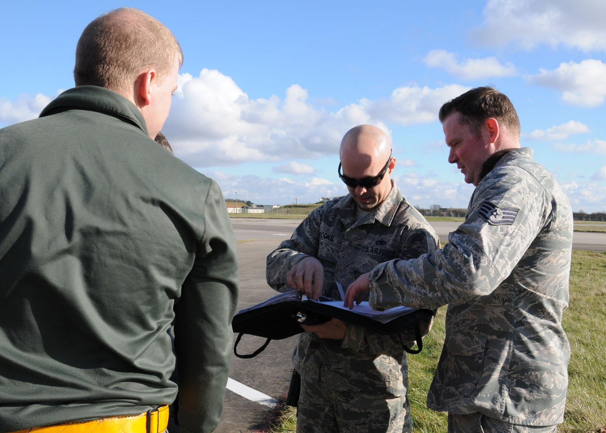 U.S. Air Force Tech. Sgt. Shannon Brooks, center, 100th Aircraft Maintenance Squadron production expeditor from Folio, Calif., reviews an aircraft forms binder which contains aircraft maintenance discrepancies and statuses Feb. 19, 2014, on RAF Mildenhall, England. Brooks improved the wash rack program by establishing a team structure, ensuring the wash teams had transportation and adequate tools, and he implemented a 30-day wash cycle. (U.S. Air Force photo by Gina Randall/Released)