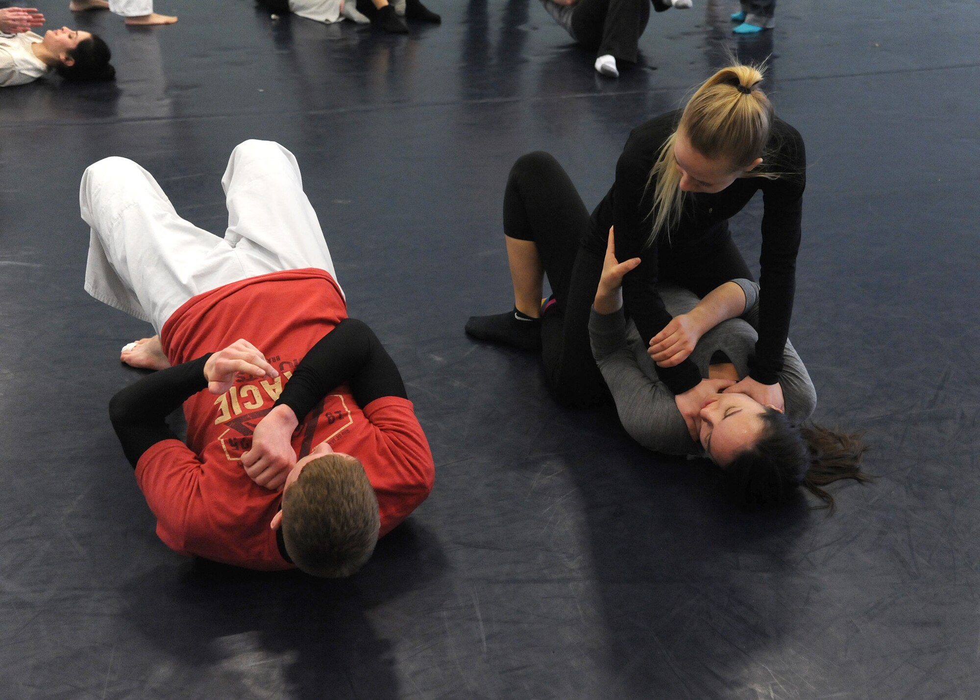 Malmstrom dependents, Ela Hale (top right) and Emily Parzynski (bottom right), watch as Senior Airman Tory Satterfield, 341st Missile Security Forces Squadron member, show them the proper way to execute a trap and roll technique during a Gracie Defense Seminar kickoff Feb. 22. During the seminar, participants were taught combat base, base get up, push base, pull base, wrist releases, one front-choke defense and a trap-and-roll technique. (U.S. Air Force photo/Senior Airman Cortney Paxton)