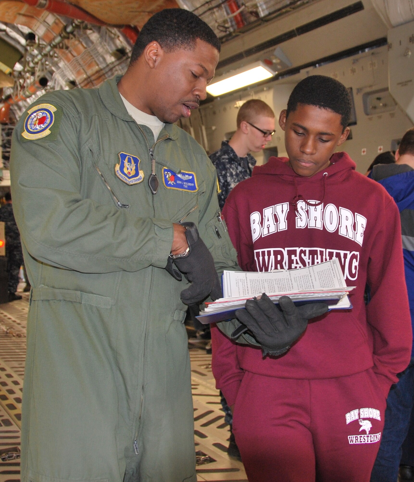 Tech Sgt. Sean McClendon, 732nd Airlift Squadron, shows his son Josiah McClendon, 13, an instruction manual detailing the procedures of pallet placement and removal during a Sea Cadet visit here Feb. 22 (U.S. Air Force photo/Senior Airman Chelsea Smith).