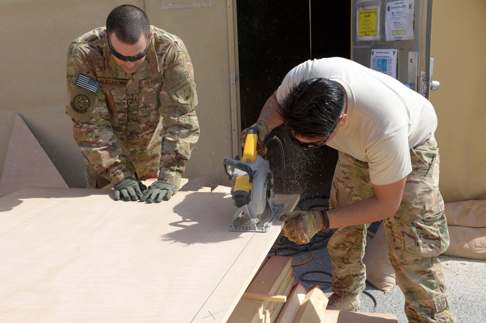 Staff Sgt. Angel Alexander holds a piece of plywood as Airman 1st Class Kristian Martinez-Felix cuts the plywood for the 31st Air Defense Artillery Brigade’s Tactical Operations Center at Al Udeid Air Base, Qatar, Feb. 24, 2014 The 577th Prime BEEF was tasked to construct a TOC to provide a robust and clear audio and visual common operating picture spanning over five nations in the Arabian Gulf region and to meet the security requirements of the 31st ADA Brigade.  Both Airmen are 577th EPBS heating, ventilation, and air conditioning technicians. Alexander is deployed from Kadena Air Base, Japan and a Philadelphia, native.  Martinez-Felix is deployed from Grand Forks, N.D., and a Phoenix, native. (U.S. Air Force photo/Senior Airman Hannah Landeros)
