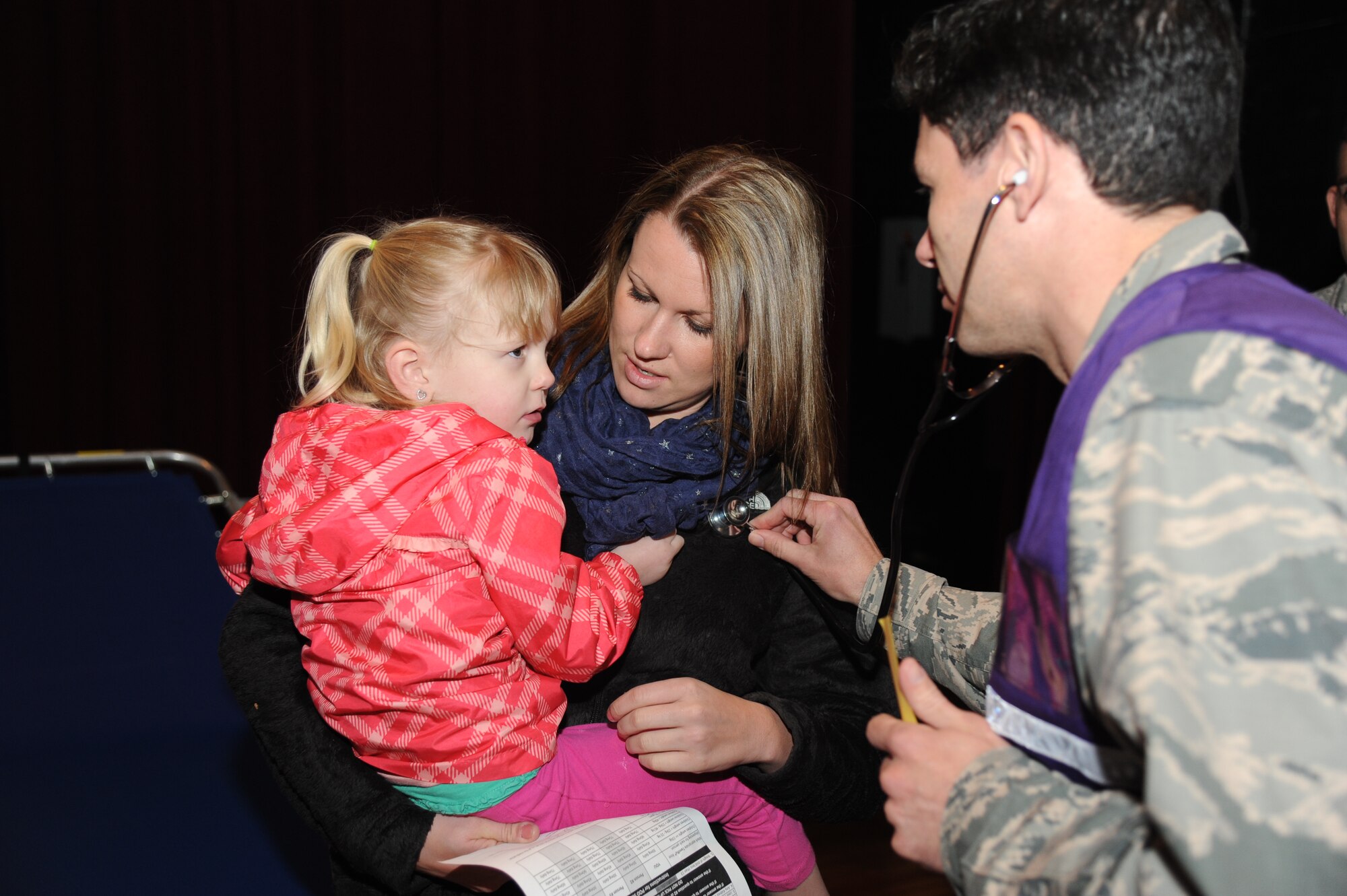Staff Sgt. Jill Wader, 334th Training Squadron, holds her daughter as she is medically examined by Capt. Michael Blancaneaux, 81st Medical Operations Squadron, during a disease containment plan and point of dispensing exercise Feb. 27, 2014, at the Welch Theater, Keesler Air Force Base, Miss. The scenario included a steep rise in the number of patients with flu-like symptoms and the medical group distributing large quantities of influenza medications and vaccinations.  (U.S. Air Force photo by Kemberly Groue)