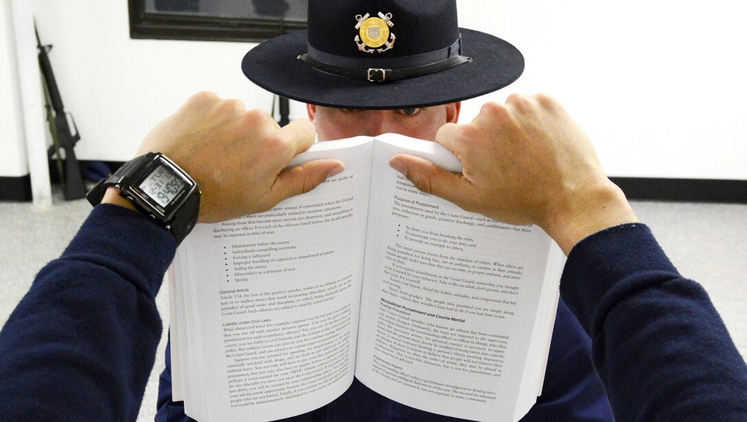 U.S. Coast Guard Petty Officer 1st Class Milton Casey peers over a Coast Guardsman's Manual at a recruiting reciting the "Purpose of Punishment" at Training Center Cape May, N.J., Dec. 31, 2013. The recruits are required to yell passages of the manual while standing with their arms fully extended. 