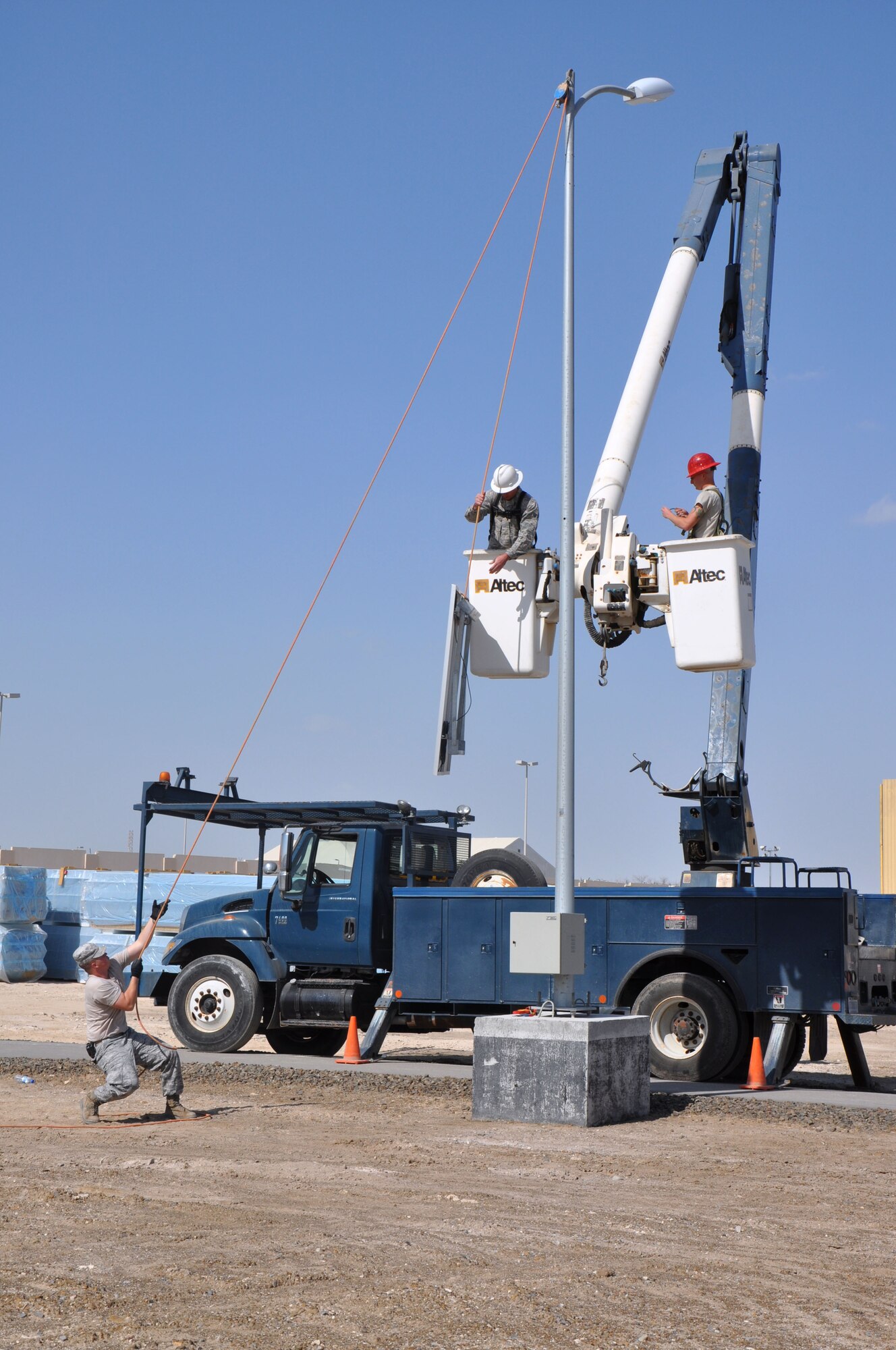 Air Force Airman 1st Class Scott Baxley pulls up a solar panel with a block and tackle for Senior Airman Jason Carniewski to mount on the light pole. All three Airmen pictured are electrical systems journeymen assigned to the 380th Expeditionary Civil Engineer Squadron. (U.S. Air Force photo by Master Sgt. April Lapetoda/Released)