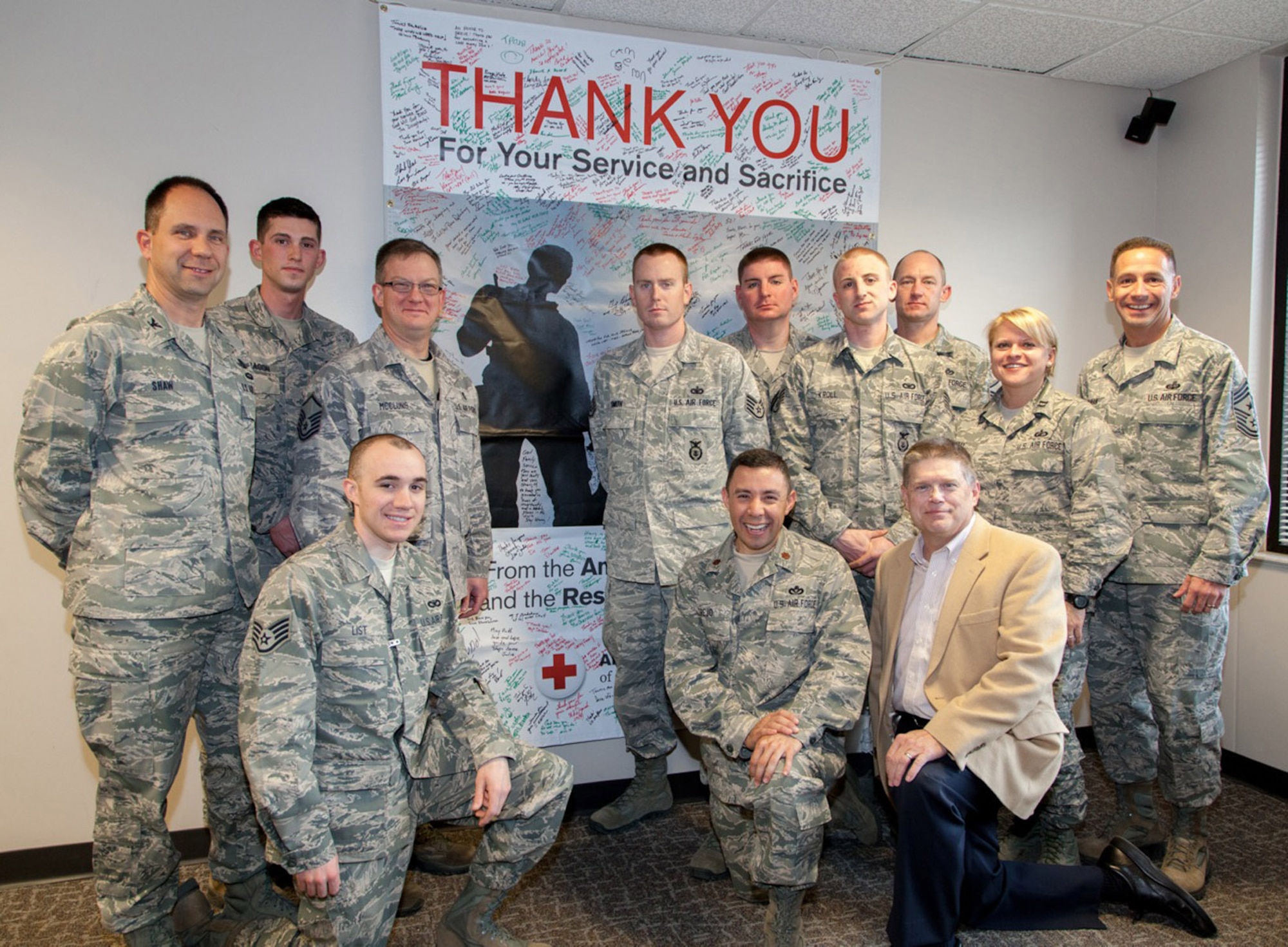 PETERSON AIR FORCE BASE, Colo. – Col. John Shaw (left), 21 Space Wing commander, and Chief Master Sgt. Rich Redman (right), 21st SW command chief, (right) accept a Thank You banner from James Griffith (kneeling), Red Cross Service to Armed Forces manager, Dec. 18. Shaw and Redman accepted the banner on behalf of service members who have deployed. The banner was posted in public forums to allow community members to sign and express their thanks and appreciation for those who serve, and have served, in America’s armed forces. (American Red Cross photo/Arnett Luce)