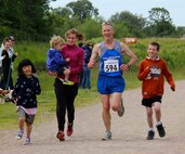 U.S. Air Force Lt. Col. Christopher Bennett, second from right, Headquarters Air Force Reservist Directorate, Air Staff, Pentagon, chief of airlift and tanker requirements, prepares to cross the finish line of the Alexander the Great half-marathon on Father's Day, June 16, 2013, at Stanwick Lakes, Northamptonshire, England. As part of a family tradition, Bennett's children – from left to right, Emma, 9; Ashton, 2; Katie Reed, 15 and Elijah, 10 – run with their dad every Father's Day. As he was running the half-marathon, and his two eldest children were running the 5 km race at the same location, all four children waited near the end of the race, hopped on the trail and ran to the finish line with him. Bennett recently completed his goal of running "20 13s" in 2013 – 20 half-marathons, the majority of which he ran while stationed at RAF Mildenhall in England. (Courtesy photo by Molly Bennett/Released)