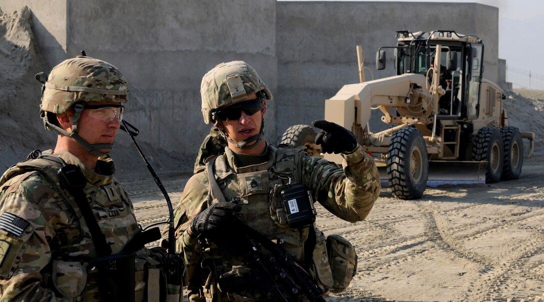 U.S. Army Staff Sgt. Brandon Bleiler, right, and U.S. Army 1st Lt. Benedict Zilka discuss future engineer training and projects for Forward Operating Base Gamberi in Afghanistan's Laghman province, Jan. 5, 2014. Behind them, an Afghan soldier uses a grader to level the area that will become the base's new expanded ammunition control point. Bleiler is assigned to the 333rd Engineer Company and Zilka is assigned to the 284th Engineer Company.