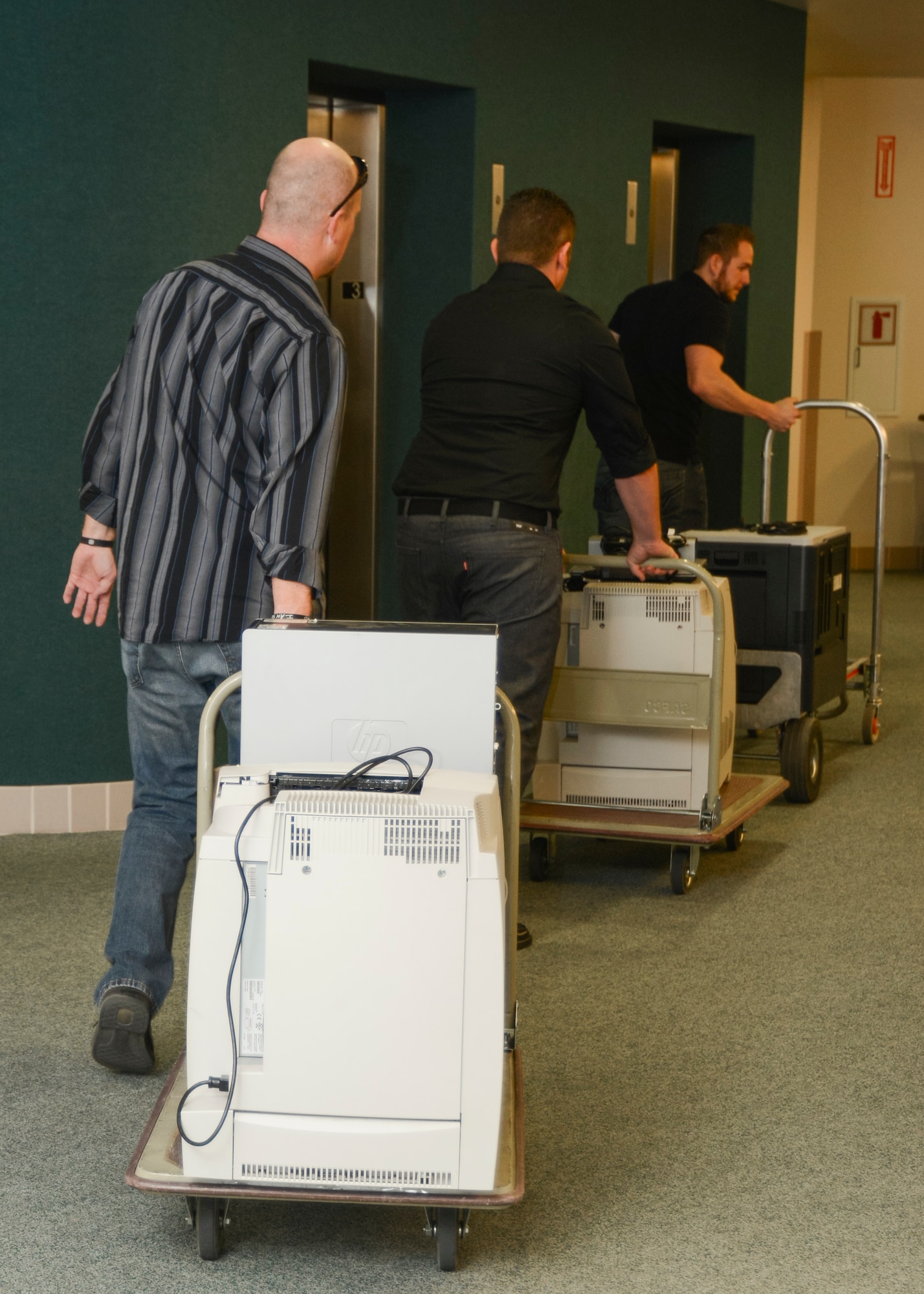 Russell Bomar (right), 412th Communications Squadron, Print Services technician leads Andrew King (center), 412th CS Print Services lead, and Andrew Gumm to the elevators with the printers collected at the 412thTest Wing Headquarters Bldg. (U.S. Air Force photo by Rebecca Amber) 