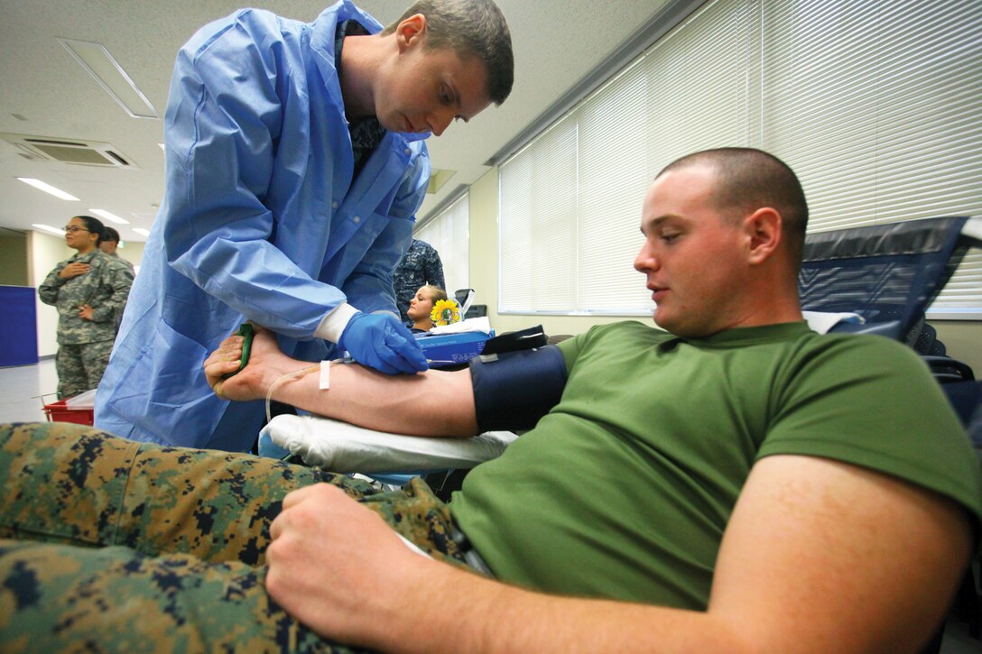 Seaman Zachary Walsh, standing, prepares to draw Cpl. Jeremy T. Marsh’s blood during a blood drive Jan. 6 at Bldg. 494 on Camp Foster. Walsh is a hospital corpsman at U.S. Pacific Command’s Armed Services Blood Bank Center. Marsh is a network defense administrator with G-6, communications, Marine Corps Base Camp Smedley D. Butler, Marine Corps Installations Pacific. (U.S. Marine Corps photo by Cpl. Alyssa N. Gunton/Released)