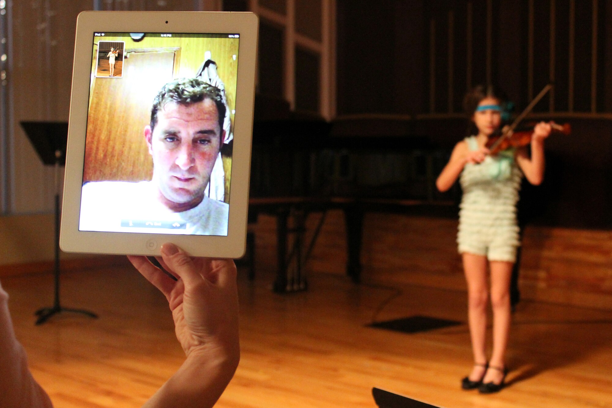 Master Sgt. Michael Morgan, 72nd Air Refueling Squadron inflight refueling evaluator, can be seen on a tablet device as he watches his daughter, Melea, play violin during a recital in Carmel, Ind., Oct. 27, 2013. Morgan kept in close contact with his family during a recent deployment to Southwest Asia. (U.S. Air Force photo illustration/Tech. Sgt. Erica Morgan)