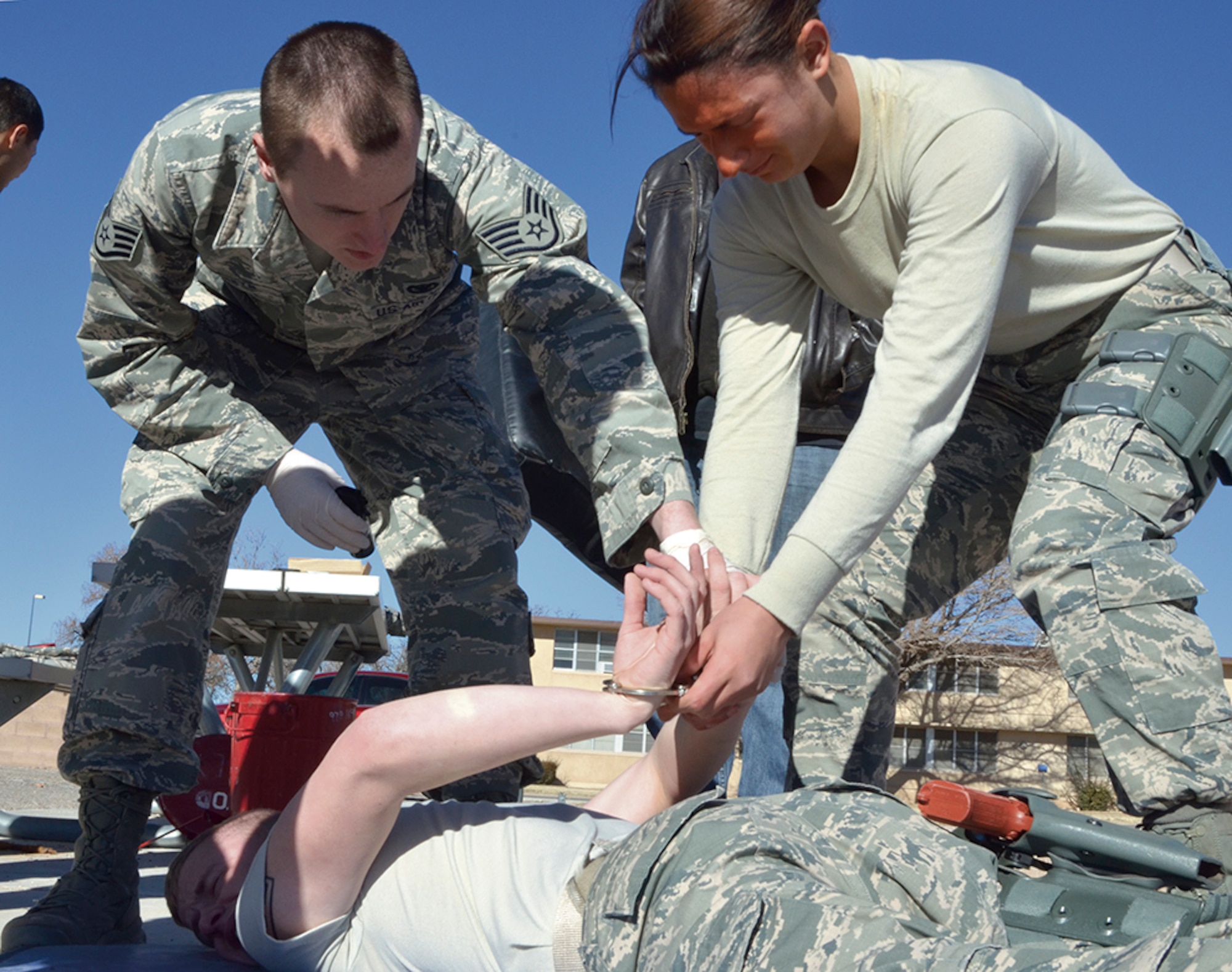 After receiving a blast of pepper spray in her face, Airman 1st Class Frankie Macfie handcuffs Airman 1st Class Blake Johnson during a 377th Security Forces Squadron training exercise. Staff Sgt. Joshua Sheets, left, checks that Macfie has properly double-locked the handcuffs. The training was done in an empty lot on the west side of Kirtland Jan. 3. (Photo by Lee Ross)