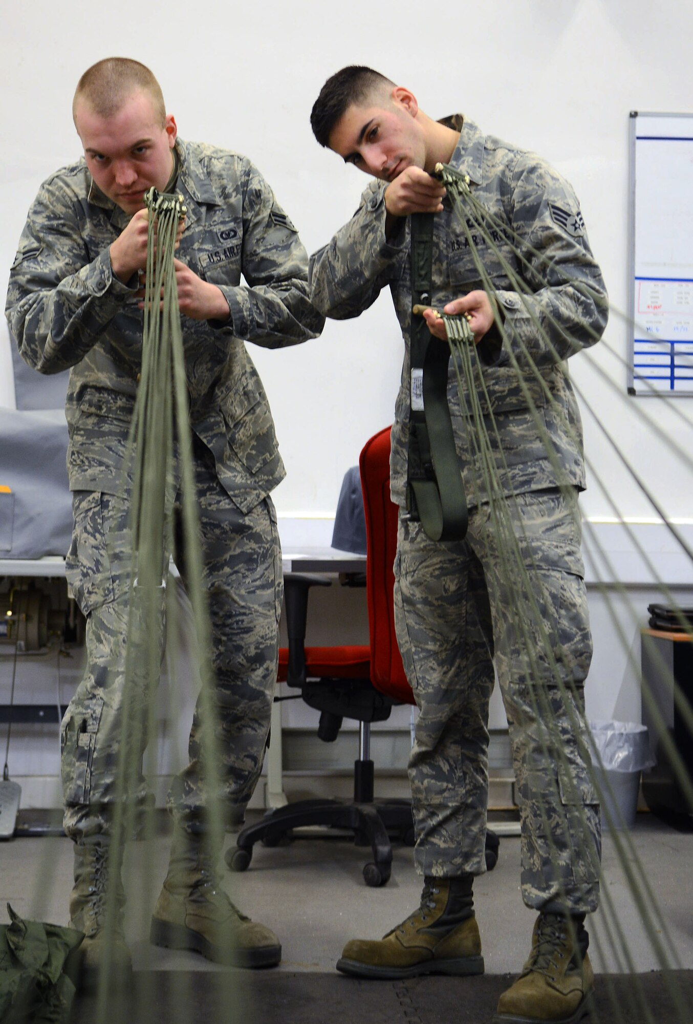 U.S. Air Force Senior Airman Joseph Cyr, right, 100th Operations Support Squadron aircrew flight equipment journeyman from Newport, R.I., trains U.S. Air Force Airman 1st Class Ian Radandt, 100th OSS aircrew flight equipment apprentice from Oshkosh, Wis., on the preparation of parachutes before they are packed Jan. 8, 2014, on RAF Mildenhall, England. Cyr earned the Square D Spotlight for exhibiting the Air Force Core Value of Service Before Self. (U.S. Air Force photo by Airman 1st Class Kyla Gifford/Released)