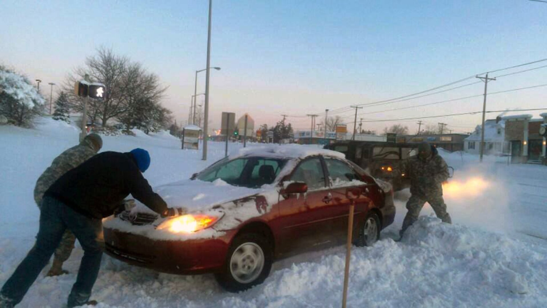 Soldiers with the 1st Battalion, 293rd Infantry Regiment Highway Assistance Team, assited by a civilian, push out a stranded mother and her child in Fort Wayne, Ind., Jan. 6, 2014.
