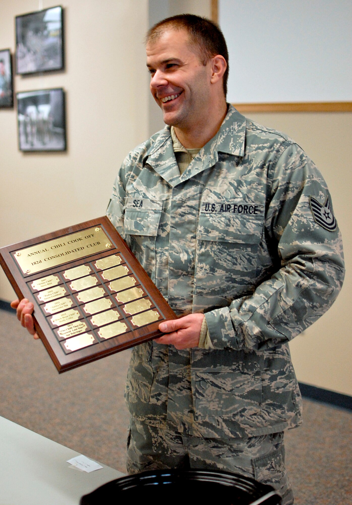 U.S. Air Force Tech. Sgt. Alex R. Sea, vehicle equipment maintenance specialist with the 182nd Logistics Readiness Squadron, displays the plaque of winners after the sixth-annual chili cook off at the 182nd Airlift Wing, Peoria, Ill., Jan. 8, 2014. The competition placed 13 contestants and their homemade chili recipes against each other to compete for best look and smell, best consistency, and best taste. Sea won in both the best consistency and most overall points categories for his Jabbo Chili recipe. He was awarded a five-year membership to the wing’s consolidated club and had his name added to the winners’ plaque. The event brought out approximately 120 unit members to sample the various white and traditional red entries, and raised $490 in support of operating the wing’s consolidated club. Sea enjoys the yearly event because he gets to have good chili with good people, he said. “It’s a good way to get out and mingle and talk to the people you don’t usually see on a day-to-day basis.” (U.S. Air National Guard photo by Staff Sgt. Lealan Buehrer/Released. Image was cropped to emphasize subject.)