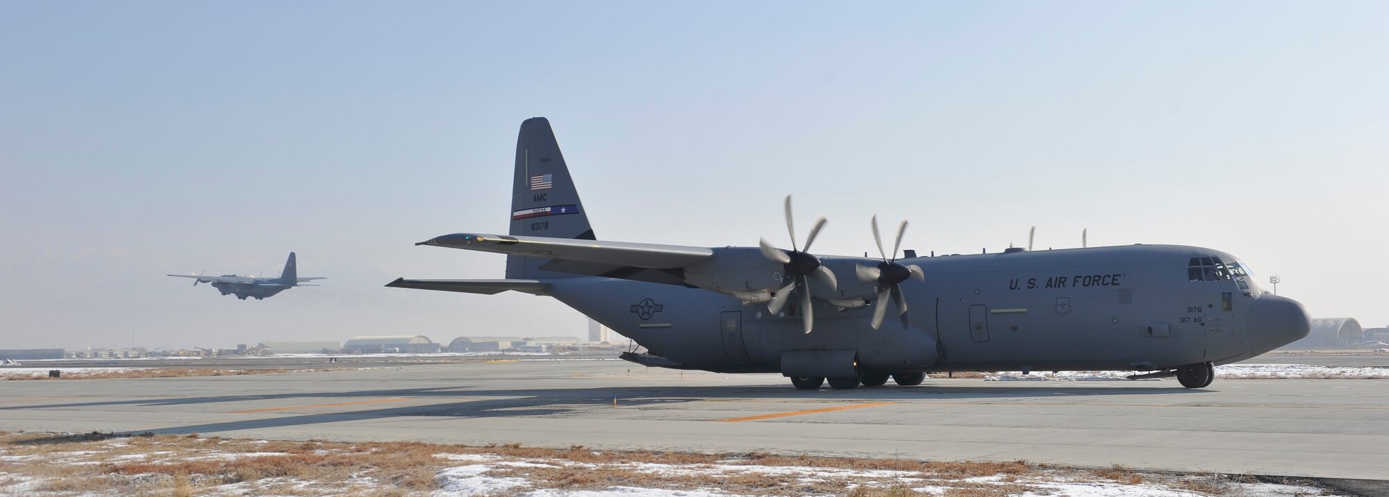 A U.S. Air Force C-130H model aircraft takes off on its last flight out of Bagram Airfield, Afghanistan, Jan. 9, 2013, while a newer C-130J model aircraft taxis in to replace it. The two aircraft were the first of the C-130H model aircraft to permanently relocate out of Bagram and the first of the C-130J models to replace it.(U.S. Air Force photo by Senior Master Sgt. Gary J. Rihn/Released)