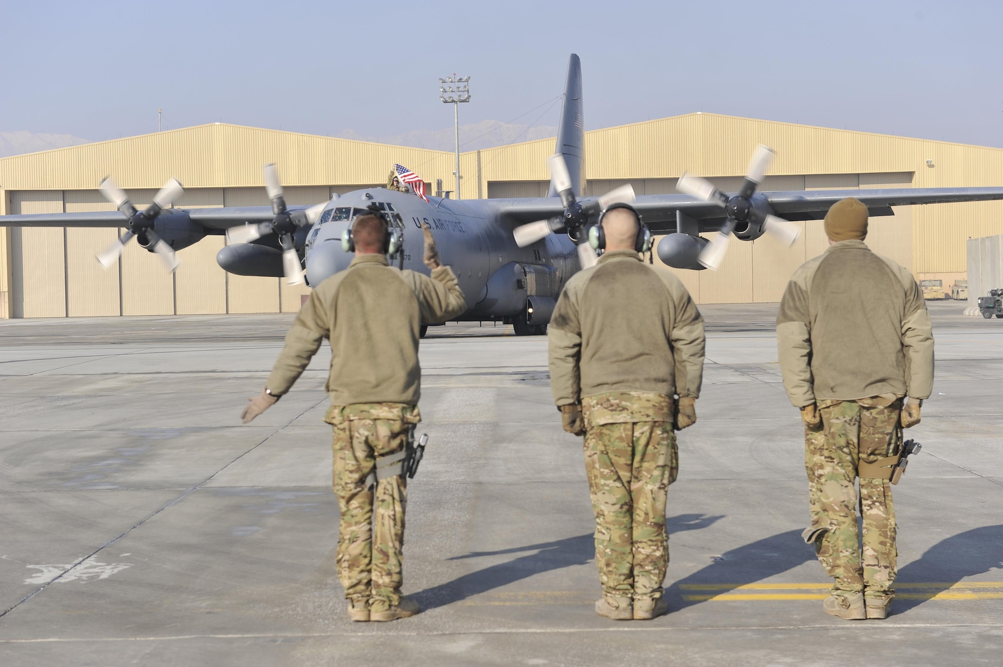 U.S. Air Force Technical Sgt. Keith LaFontaine, accompanied by Senior Airman Larry Webster and Technical Sgt. Richard Mulhollen, marshals out a C-130 before its flight out of Bagram Airfield, Afghanistan, Jan. 9, 2013. The aircraft was the first of the C-130H model aircraft to permanently relocate out of Bagram to make room for the newer C-130J model aircraft.(U.S. Air Force photo by Senior Master Sgt. Gary J. Rihn/Released)