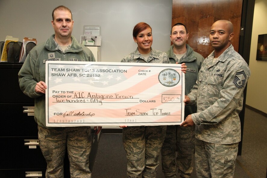 U.S. Air Force Master Sgt. James Henderson (Left), Top 3 member at large, Master Sgt. Timothy Rischak (center right), Top 3 member, and Senior Master Sgt. Demetrius Jones (right), Top 3 President, present Airman 1st Class Antigone Brown, 20th Force Support Squadron evaluations technician, with a 250 dollar scholarship from the Top 3 organization, Shaw Air Force Base, S.C., Jan 9, 2014. Brown won one of two scholarships given by the Top 3. (Courtesy photo)