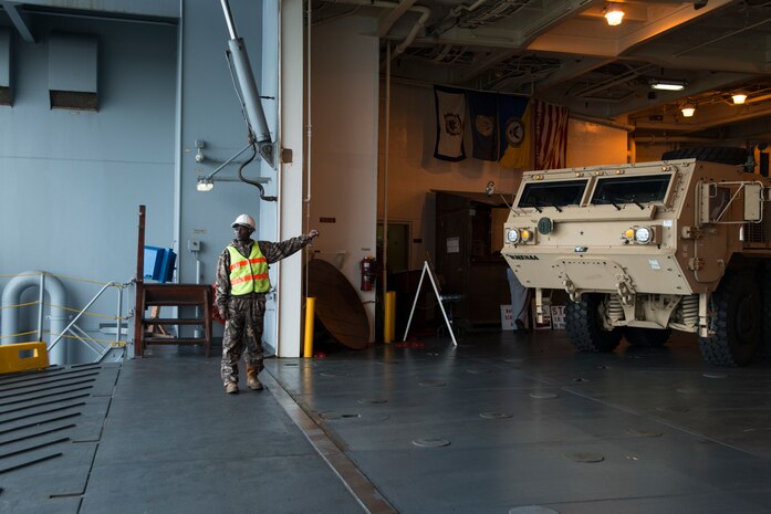 Darriel Porcher, International Longshoreman Association flagman, holds a Mine-Resistant Ambush Protected vehicle on station onboard the USNS Pomeroy (T-AKR-316), Jan. 10, 2014, at the Joint Base Charleston – Weapons Station, S.C.  The Pomeroy is used to preposition United States military combat equipment and combat support equipment overseas and for re-supplying U.S. armed forces with necessary equipment and supplies during national crises. (U.S. Air Force photo/Senior Airman Ashlee Galloway)