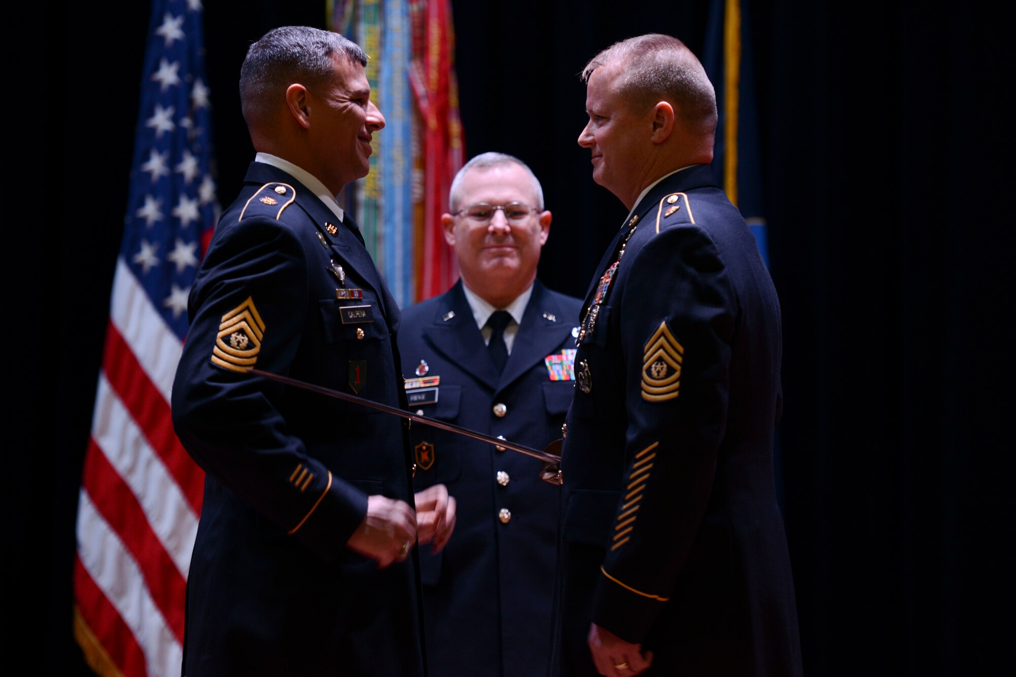 From left, U.S. Army Sgt. Maj. John Calpena, U.S. Army Training and Doctrine Command Initial Military Training command sergeant major, passes the sword to Sgt. Maj. Dennis Woods, incoming IMT command sergeant major, at a change of responsibility ceremony inside Wylie Theater at Fort Eustis, Va., Jan. 10, 2014. The passing of the sword signifies the transition of changing the senior enlisted advisor of the command. (U.S. Air Force photo by Staff Sgt. Ciara Wymbs/Released)
