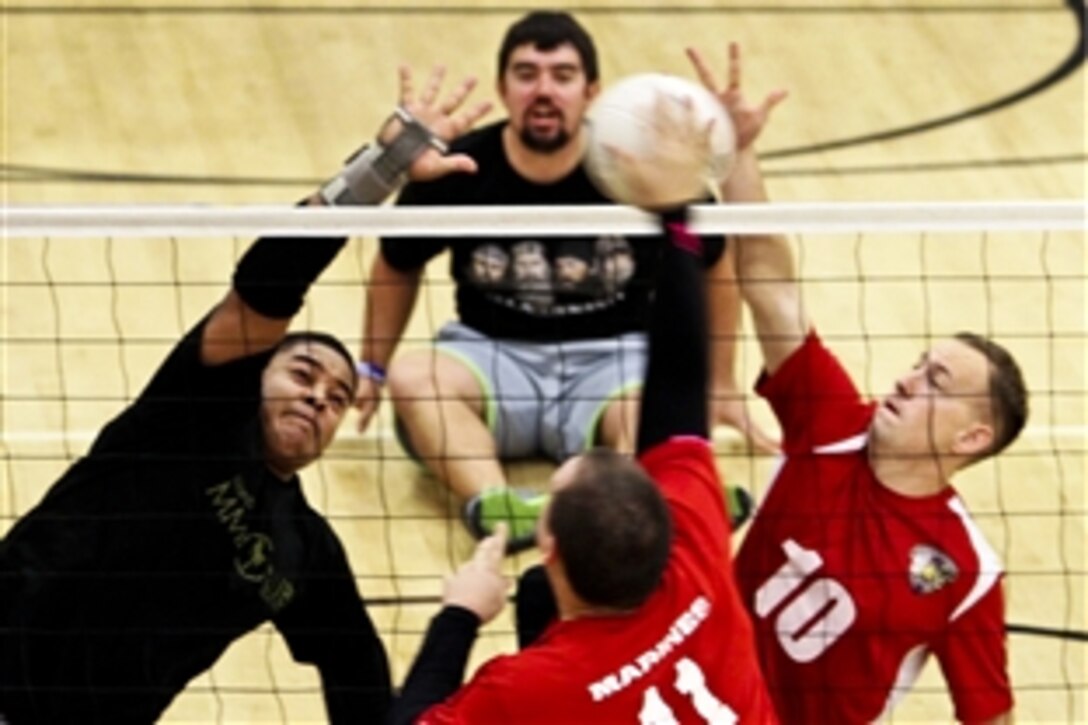 Marine Corps Cpl. Gabriel Beltres, left, and Cpl. Benjamin McCrosky, right, attempt to block a hit by Marine veteran Zach Blair in a scrimmage match during the Wounded Warrior Regiment Sitting Volleyball Camp at the University of Central Florida in Orlando, Jan. 13, 2014. Marines and Marine veterans participating in the camp will enhance their skills in the areas of hitting, passing, serving and defensive techniques. 