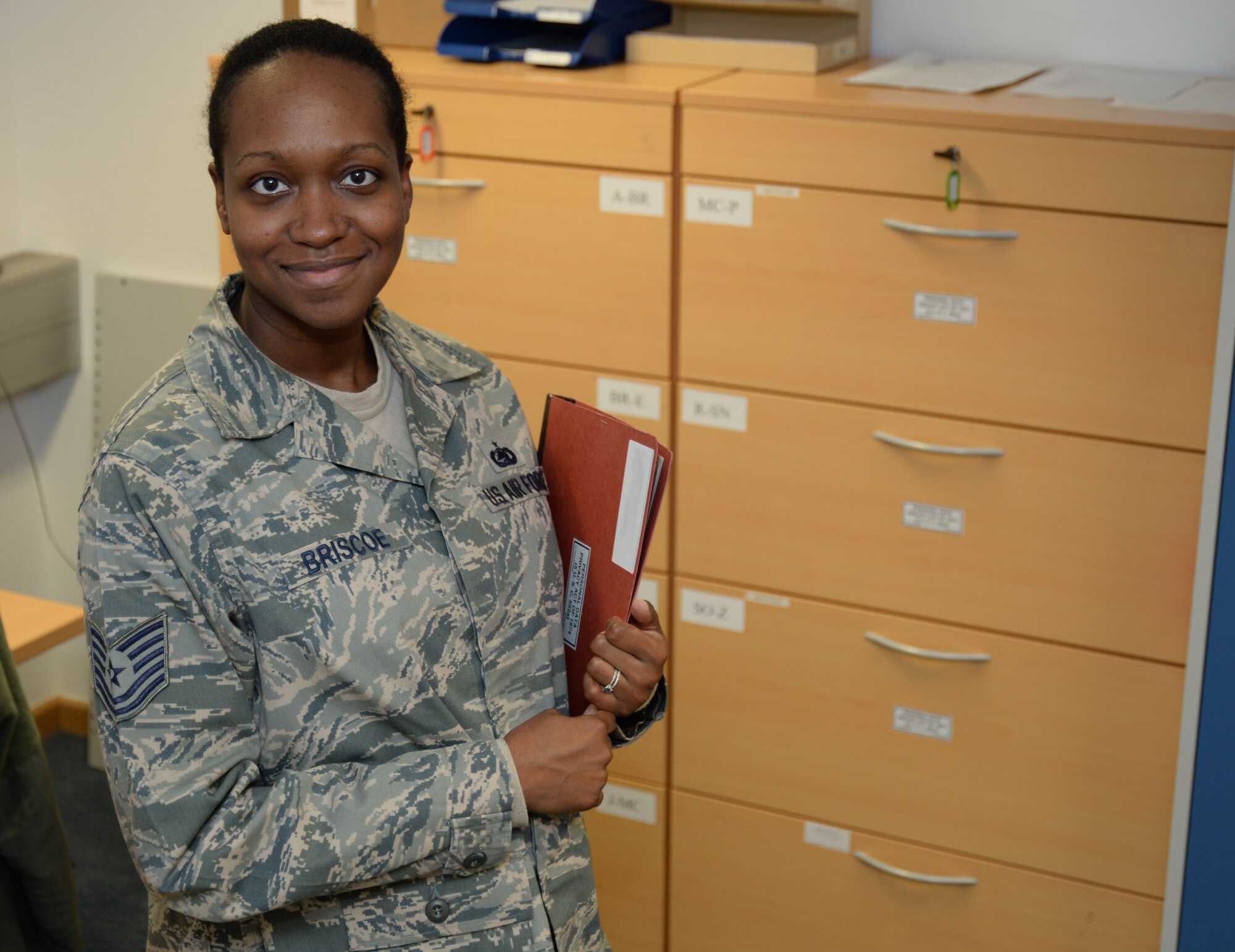 SPANGDAHLEM AIR BASE, Germany -- Tech. Sgt. Tena Briscoe, unit deployment manager of 606th Air Control Squadron of Baltimore, Md., poses next to her file cabinet at her squadron's headquarters Jan. 13, 2014. As UDM, Briscoe ensures each individual Airman is prepared for pending deployments and for their eventual return back to their home station. (U.S. Air Force illustration by Staff Sgt. Joe W. McFadden / Released)
