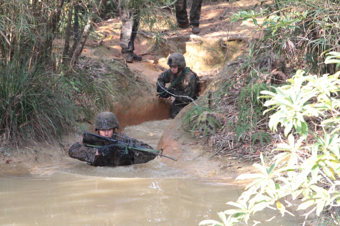 Lance Cpl. Remington Ostrem wades into water as Cpl. Ronald Mitchell follows closely behind during an endurance course Jan. 12 at the Jungle Warfare Training Center on Camp Gonsalves. Ostrem is a machine gunner, and Mitchell is a mortarman. Both  Marines are with Company K, 3rd Battalion, 1st Marine Regiment, currently assigned to 4th Marine Regiment, 3rd Marine Division, III Marine Expeditionary Force, under the unit deployment program. (U.S. Marine Corps by photo by Lance Cpl. Stephen D. Himes/Released)