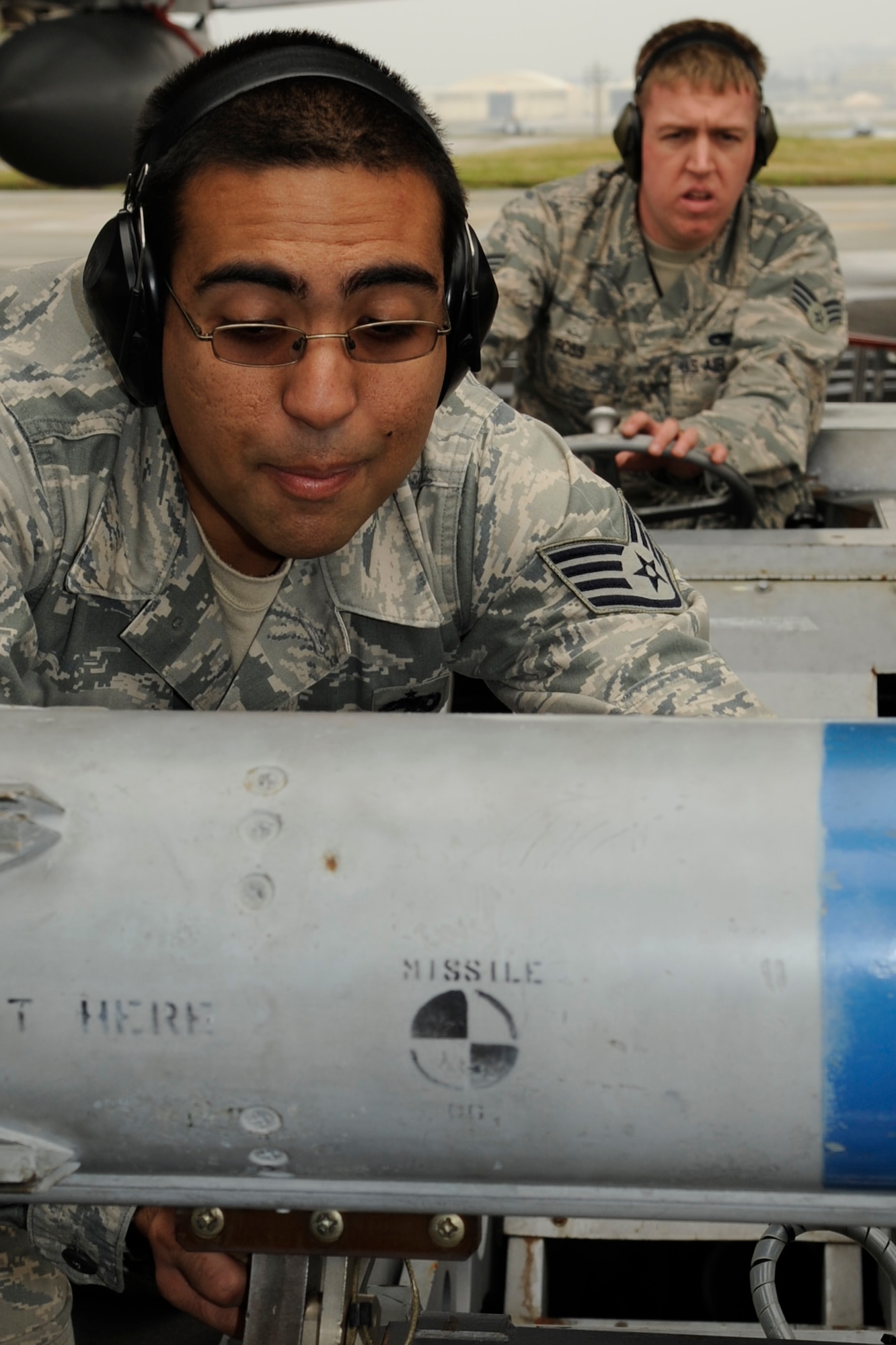 U.S. Air Force Senior Airman Zachary Ross, 67th Aircraft Maintenance Unit weapons load crew member, guides a bomb loader into place as Staff Sgt. Emad Hamedeyyeh, 67th AMU weapons load crew member, straps a missile onto the loader during a quarterly weapons load competition on Kadena Air Base, Japan, Jan. 13, 2014. The teams were inspected on safety, reliability and technical orders of loading the F-15 Eagle. (U.S. Air Force photo by Senior Airman Marcus Morris)