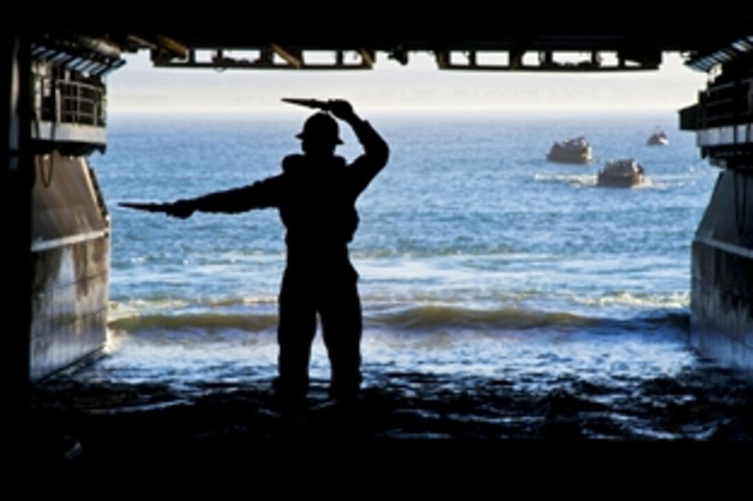 A U.S. signalman aboard the amphibious assault ship USS Makin Island communicates with lighter, amphibious resupply, cargo vehicles during the ship's well deck operations in the Pacific Ocean, Jan. 13, 2014. The Makin Island is conducting sea trials.