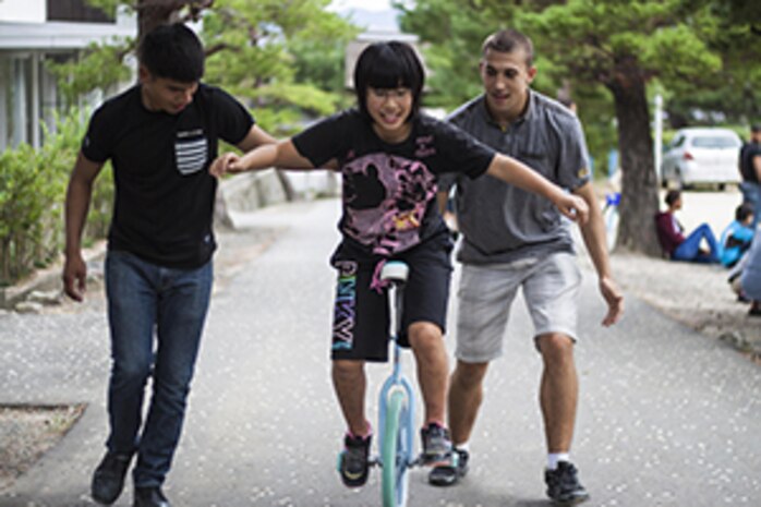 Lance Cpl. Carlos Santos, left, an aviation technician with Marine Attack Squadron 214, and Lance Cpl. Mitchell Jameson, an S-2/S-6 clerk with Combat Logistics Company 36, assist a child from a Yamaguchi city children’s home in riding a unicycle during a Single Marine Program trip, Oct. 19, 2013. The SMP provides several opportunities throughout the year for service members to give back to the local community.