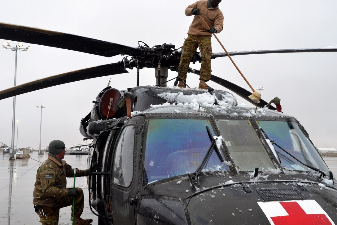 U.S. Army Spcs. Jimmy Rop, top, and James Verlander prepare to remove ice from a UH-60 Black Hawk medevac helicopter after a snowfall on Kandahar Airfield, Afghanistan, Jan. 8, 2014. Rop and Verlander are crew chiefs assigned to Company C, 2nd General Support Aviation Battalion, 1st Aviation Regiment.
