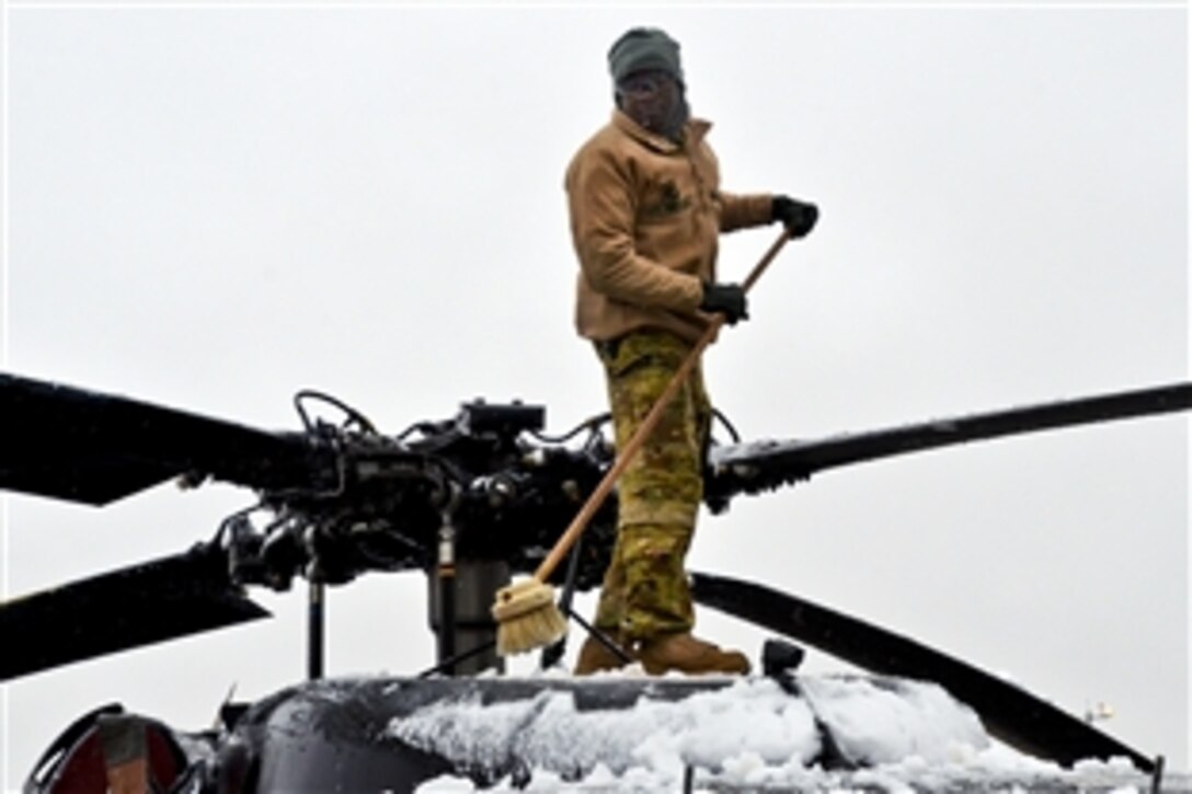 U.S. Army Spc. Jimmy Rop uses a push broom to remove snow from a UH-60 Black Hawk medieval helicopter on Kandahar Airfield, Afghanistan, Jan. 8, 2014. Rop is a crew chief assigned to Company C, 2nd General Support Aviation Battalion, 1st Aviation Regiment.