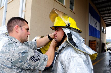 U.S. Air Force Tech. Sgt. Clive Chipman, Soto Cano Fire Department Assistant Chief of Operations, assists Gustavo Triminio, a member of a Honduran fire brigade, in donning firefighting equipment during a fire muster hosted by the firefighters of Joint Task Force-Bravo's 612th Air Base Squadron, Jan. 16, 2014.  Thirty members of local Honduran fire brigades and volunteer fire departments participated in the fire muster, which served to bring U.S. and Honduran firefighters together to build camaraderie, engage in training, and take part in friendly competition.  (Photo by Martin Chahin)