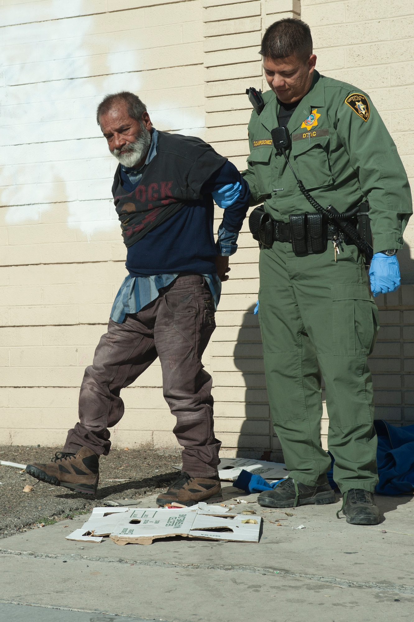 Aden Ocampogomez, Las Vegas Metropolitan Police Department police officer, helps a homeless man up before putting him in the back of his police car for drinking alcohol on the sidewalk in downtown Las Vegas Jan. 14, 2014. It is against the law to drink alcohol on the street while not on a casino’s property. (U.S. Air Force photo by Airman 1st Class Timothy Young)