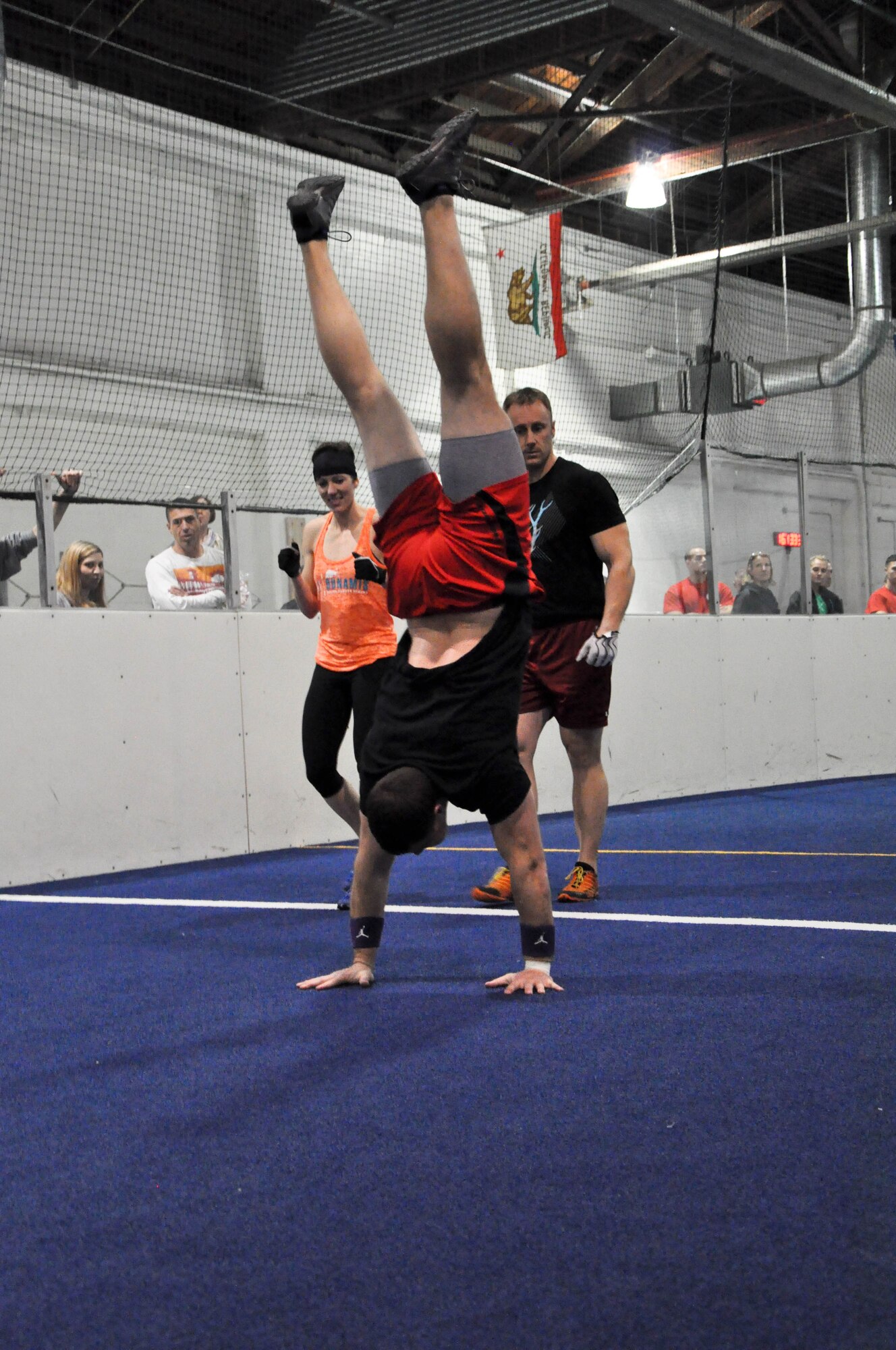 Amy Peterson and Kristian Voth from CrossFit Dunamis in Souix Falls, SD, cheer on Chris Peterson who completes a handstand walk during the championship workout for the RX division of the 2014 TactFit Games at the Offutt Field House Jan. 19. Teams came from across Nebraska, Iowa, South Dakota and Missouri to compete in the competition. (U.S. Air Force Photo by 2nd Lt. Carly A. Costello/Released)