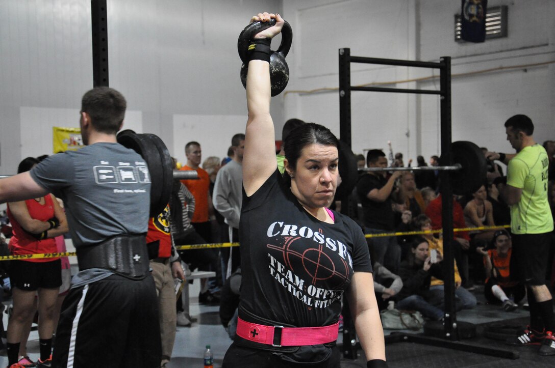 Carly Height with Team Offutt Tactical Fitness holds a 35-pound kettle bell while her partner, Angie Hobbs rows on the rowing machine during the second workout of the 2014 TactFit Games at the Offutt Field House Jan. 19. During the second workout, two team members had seven minutes to row for a calorie count, while their partner holds a kettle bell above their head. Once the kettle bell breaks the plane of the head, the partner rowing had to stop until the kettle bell was lifted again. (U.S. Air Force Photo by 2nd Lt. Carly A. Costello/Released)