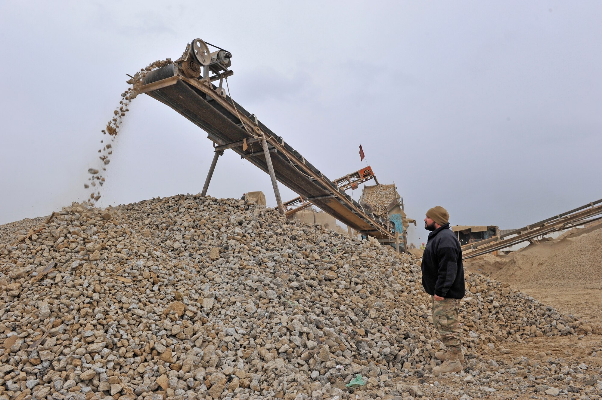 Nick Higgins, a U.S. Air Force civilian, watches the discharged material coming off of a rock crushing machine on Bagram Airfield, Afghanistan, Jan. 21, 2014. Higgins, a native of Cummings, Ga., and deployed from Robins Air Force Base, Ga., is the production manager for an operation that crushes stone and recycled concrete for use as fill and walking path surfaces on base.(U.S. Air Force photo by Senior Master Sgt. Gary J. Rihn/Released)