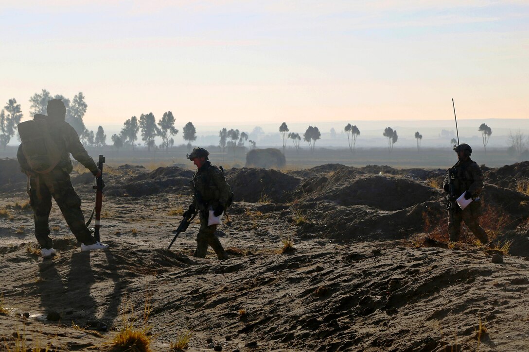 An Afghan commando, left, watches as a U.S. sailor, center, and a U.S. Special Forces soldier carry bags of suspected illegal drugs found during a clearing operation in Dewai Kalay village in the Maiwand district in Afghanistan's Kandahar province, Jan. 14, 2014. The sailor is an explosive ordnance disposal technician.