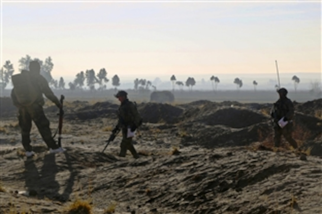 An Afghan commando, left, watches as a U.S. sailor, center, and a U.S. Special Forces soldier carry bags of suspected illegal drugs found during a clearing operation in Dewai Kalay village in the Maiwand district in Afghanistan's Kandahar province, Jan. 14, 2014. The sailor is an explosive ordnance disposal technician.