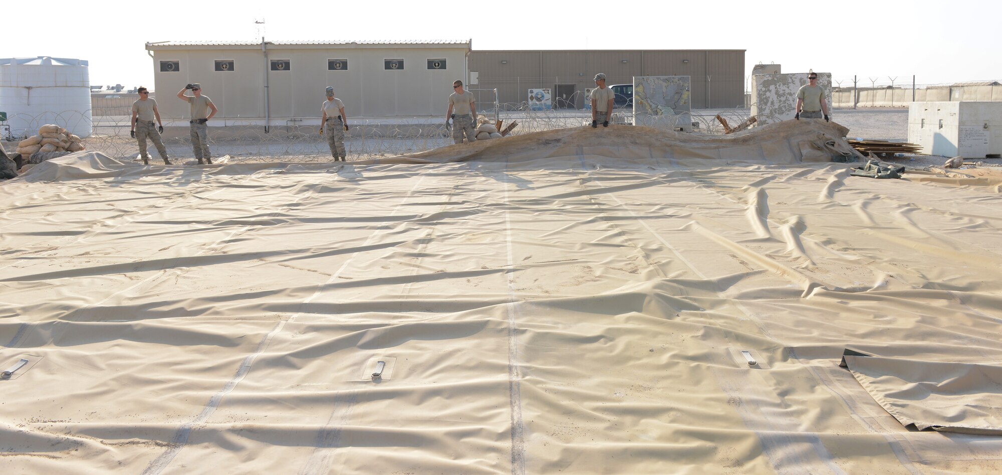 Airmen from the 379th Expeditionary Civil Engineer Squadron prepare to fold a tent during Operations Town Demobilization at Al Udeid Air Base, Qatar, Jan. 21, 2014. The 379th ECES leads the way to accomplish the project called Ops Town Demobilization with a crew of nearly 320 Airmen. The goal of the project is to move all equipment, personnel and temporary facilities in the area to a new location on base so the land can be returned to the host nation. (U.S. Air Force photo/Senior Airman Hannah Landeros)