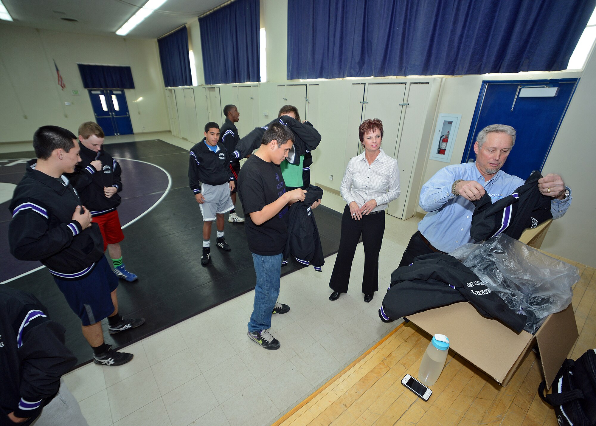 INQU president Ray Wilkens and INQU CEO Lori Wilkens (right) recently surprised and presented the Desert High School wrestling team with a set of warm-up uniforms that they donated during a team practice session on Jan. 21. Ray and Lori Wilkens had children who previously attended and graduated from DHS and wanted to give back to their local community by donating to one of the five self-funded sporting teams at DHS. (U.S. Air Force photo by Jet Fabara)