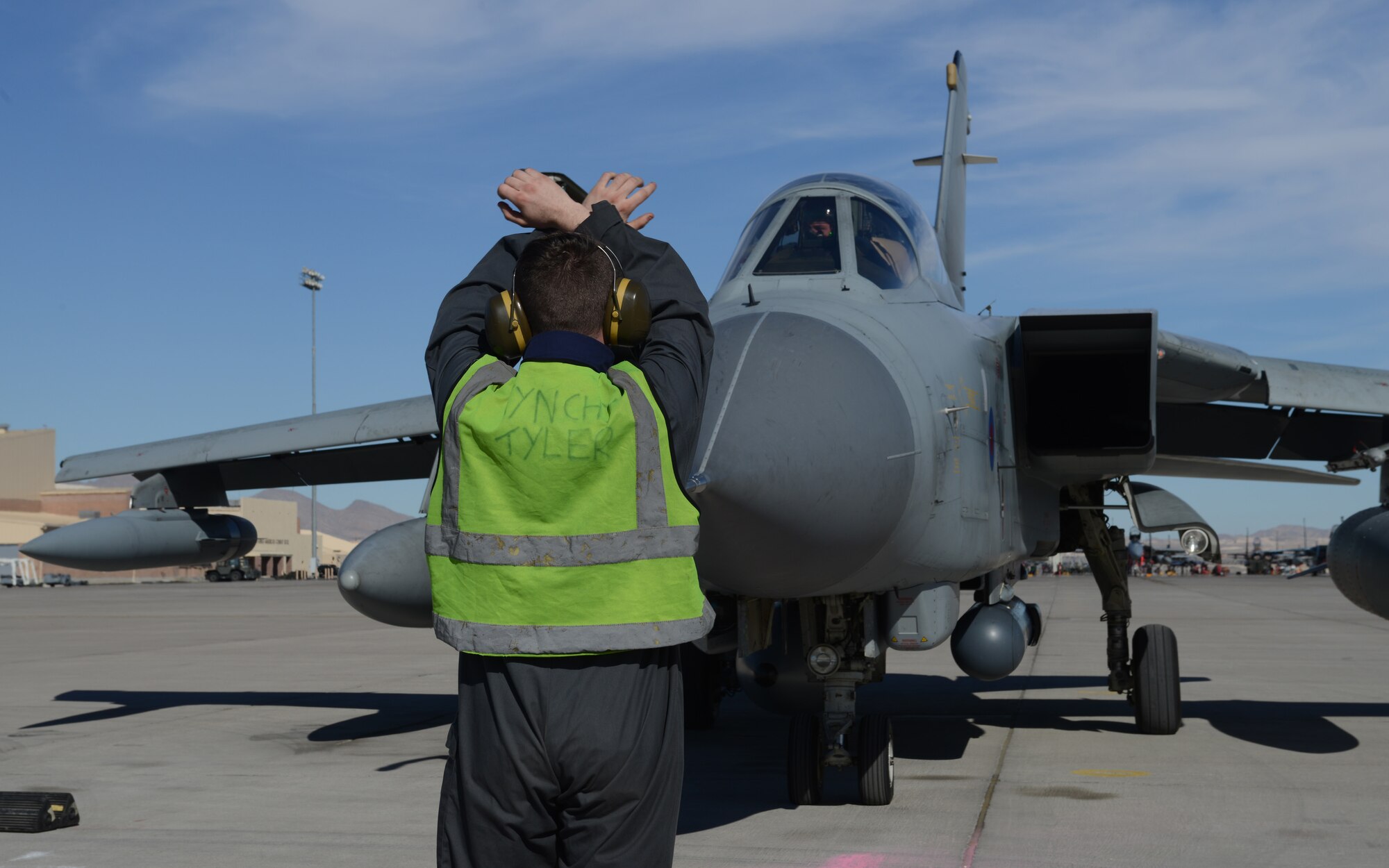 British Royal Air Force Senior Aircraftman Tyler Kerridge uses hand signals to halt a Tornado GR4 upon its arrival at Nellis Air Force Base, Nev., Jan. 22, 2013. Members of the IX (B) Squadron arrived later in the day in preparation for Red Flag 14-1. (U.S. Air Force photo by Senior Airman Benjamin Sutton/Released)
