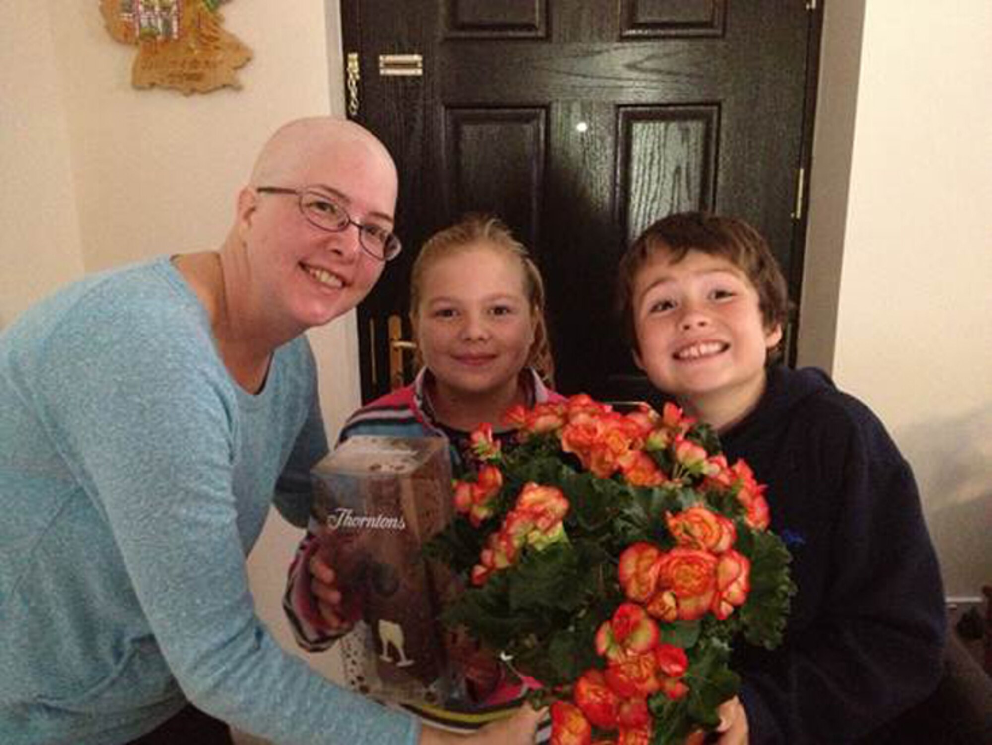 RAF ALCONBURY, United Kingdom - AnnaLee Casto (middle) and Hadyn Pollard (right) [daughter of Master Sgt. Rocky Casto and son of Mater Sgt. Nathan Pollard, 423rd ABG first sergeants] present Bonnie Ogden with flowers and chocolate they bought with money they earned by setting up a lemonade stand in their front yard. (Photo courtesy Chief Master Sgt. Michael Ogden)