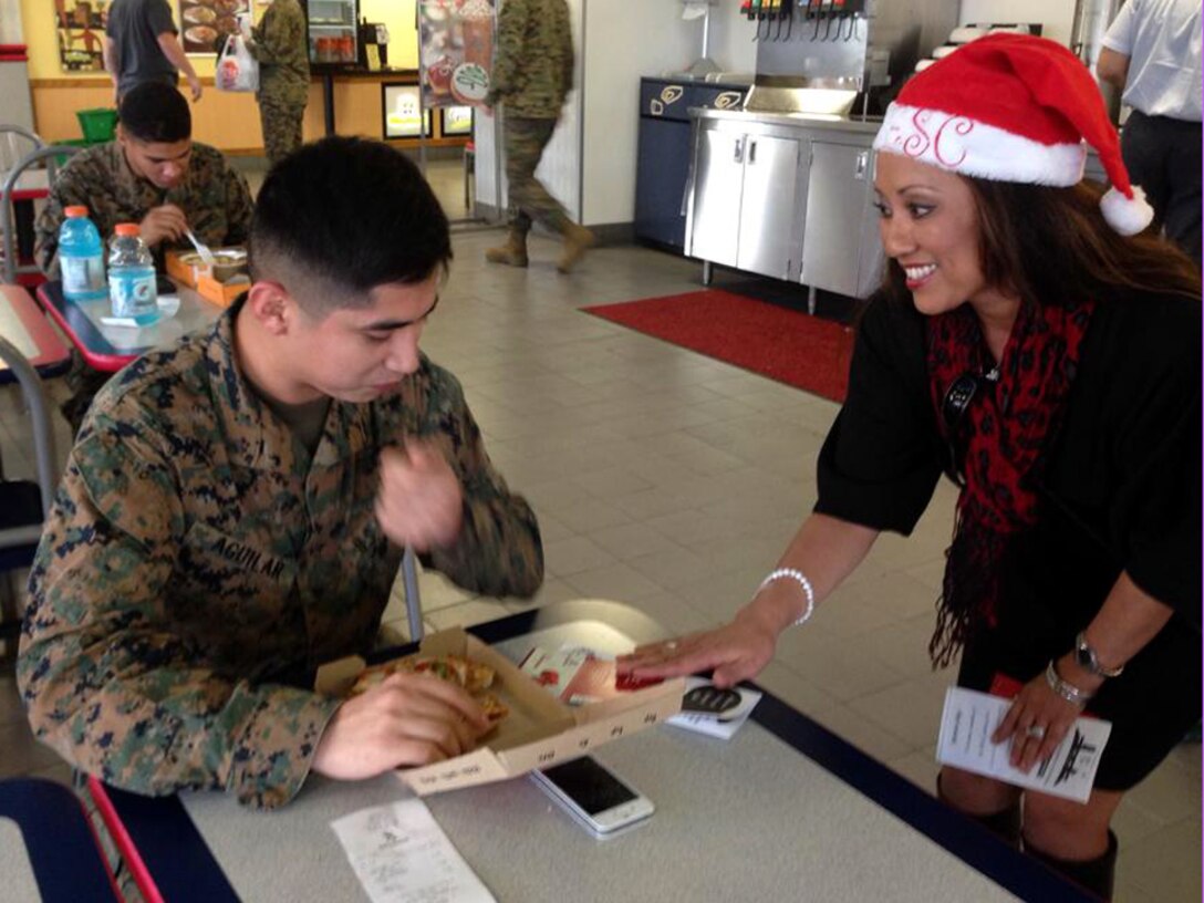 Rosalie Asuncion-Starr, Okinawa Enlisted Spouses Club president, surprises a U.S. Marine with a free gift card on Camp Foster, Japan, Dec. 19, 2013. The OESC donated $1,600 in cash and gift cards at installations throughout the island, paying for groceries, haircuts and meals to support active duty service members and their spouses. (Courtesy photo)