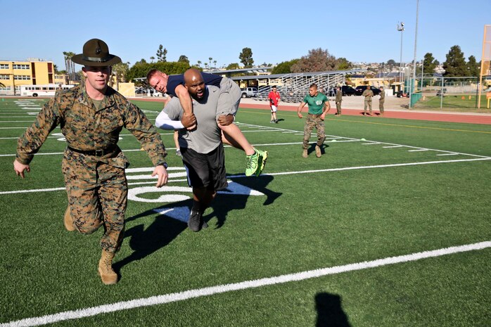 Sgt. Mark A. Peters, drill instructor, 3rd Recruit Training Battalion, runs with Herbert House, a post-secondary college and career advisor, William J. Bogan High School, as he fireman carries an educator during the Combat Fitness Test aboard the depot, Jan. 14. Drill instructors attempted to motivate each individual as they progressed through the CFT.