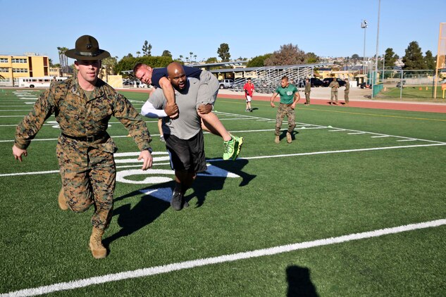 Sgt. Mark A. Peters, drill instructor, 3rd Recruit Training Battalion, runs with Herbert House, a post-secondary college and career advisor, William J. Bogan High School, as he fireman carries an educator during the Combat Fitness Test aboard the depot, Jan. 14. Drill instructors attempted to motivate each individual as they progressed through the CFT.