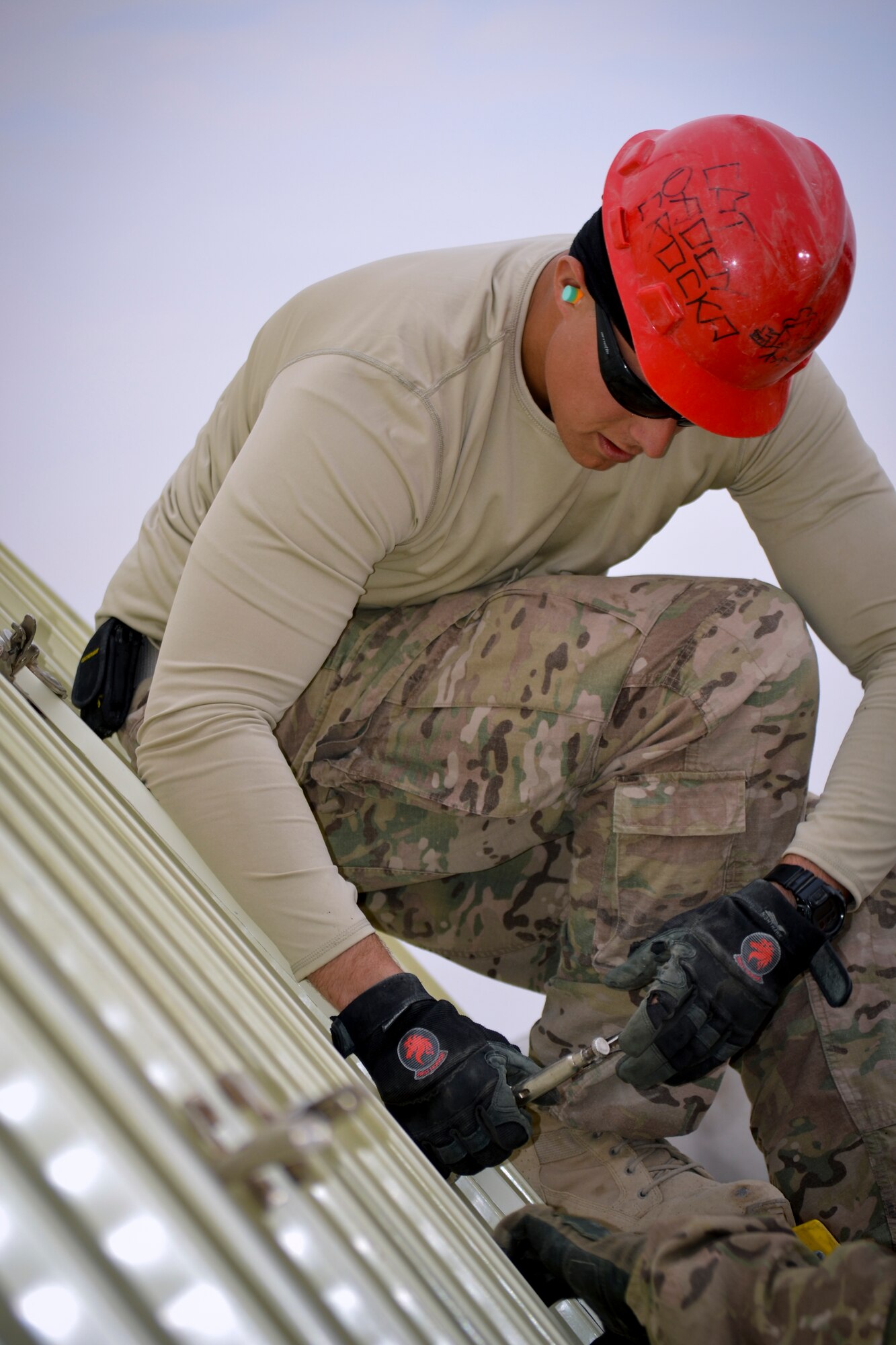 Senior Airman Clayton Crocker, a structures technician with the 557th Red Horse Squadron, 1st Expeditionary Civil Engineer Group based at Al Udeid, Qatar attaches clamps to hold pieces of a K-Span rapidly erectable structure in place during construction.  The Red Horse team was forward deployed to The Rock at the request of the 386th Expeditionary Civil Engineer Squadron to build the structure to house  power production Airmen and their generators.  The structure is replacing older, temporary facilities and will add capability and increase quality of life for the 386th CES Airmen.  (U.S. Air Force photo by Senior Master Sgt. Pamela Anderson)