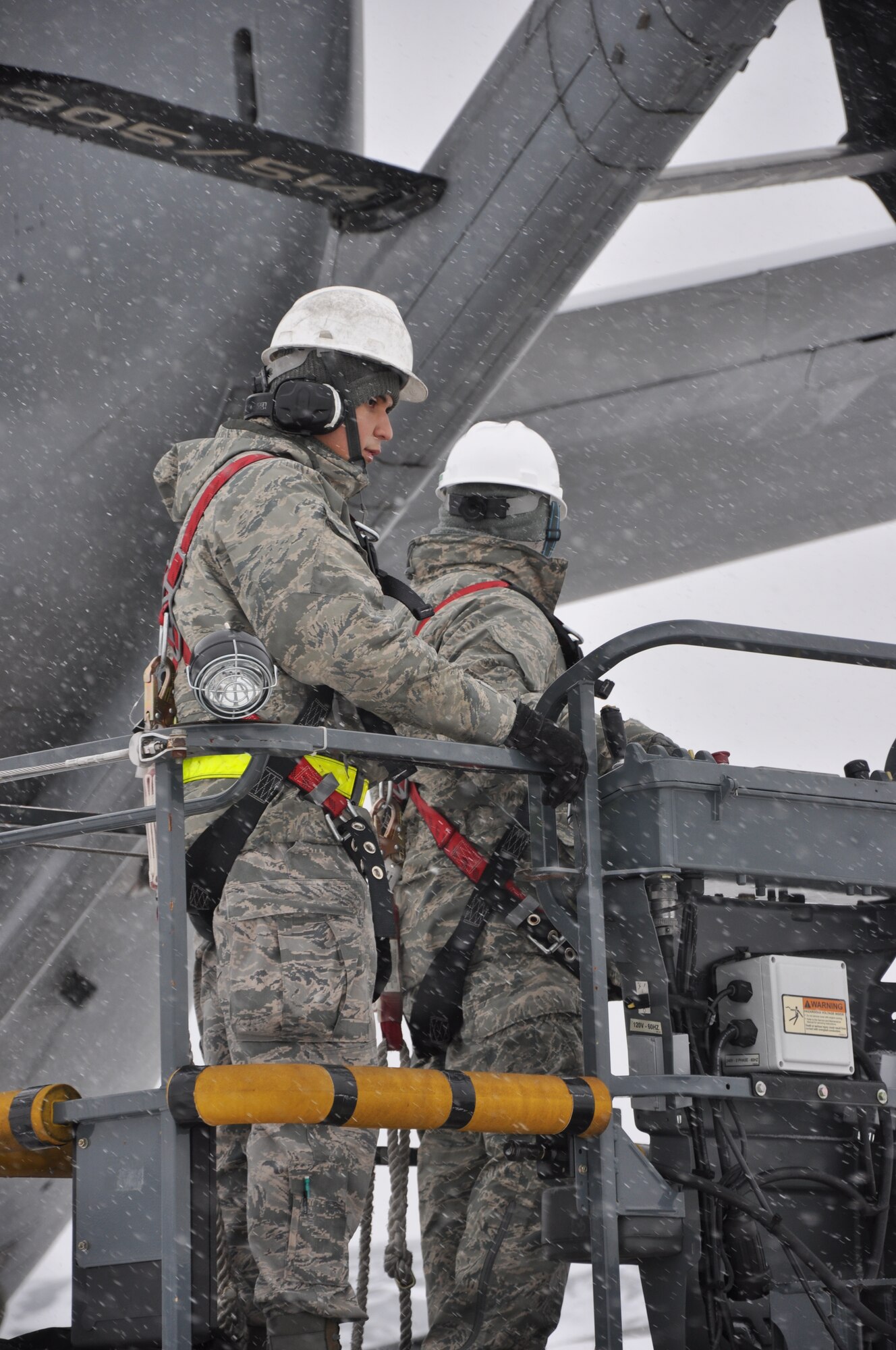 Tech Sgt. David Delitta and Senior Airman Alejandro Enriquez of the 714th Aircraft Maintenance Squadron are lowered down after installing engine covers for a KC-10 Extender aircraft during snow removal efforts here Jan. 25 (U.S. Air Force photo/Tech Sgt. Jonathan White).
