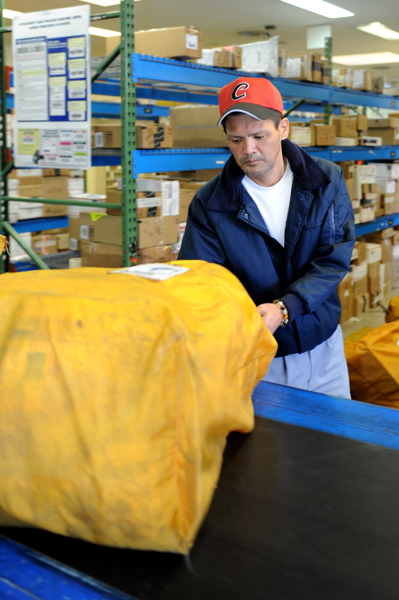 Ikemiya Tsuyoshi, 18th Communications Squadron post office worker, grabs a parcel bag from a conveyor belt at the post office on Kadena Air Base, Japan, Jan. 23, 2014. The post office delivers approximately 3 million pounds of mail a year and provides service for 27,000 customers on Okinawa. (U.S. Air Force photo by Airman 1st Class Hailey R. Staker) 