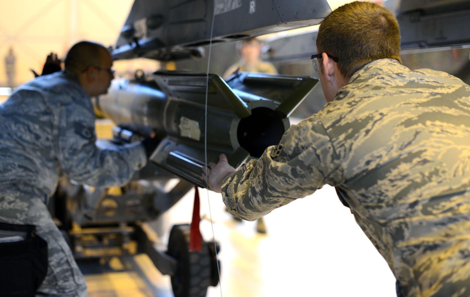 (From left) Staff Sgt. Brandon Ramos, 31st Aircraft Maintenance Squadron weapons load crew chief, and Airman 1st Class Jonathan Picher, 31st AMXS weapons load crew member, guides a munition to the wing of an F-16 Fighting Falcon during an annual weapons load crew competition Jan. 23, 2014, at Aviano Air Base, Italy.  The winning team will be announced during the Maintenance Professional of the Year Banquet. (U.S. Air Force photo/Airman 1st Class Deana Heitzman)      