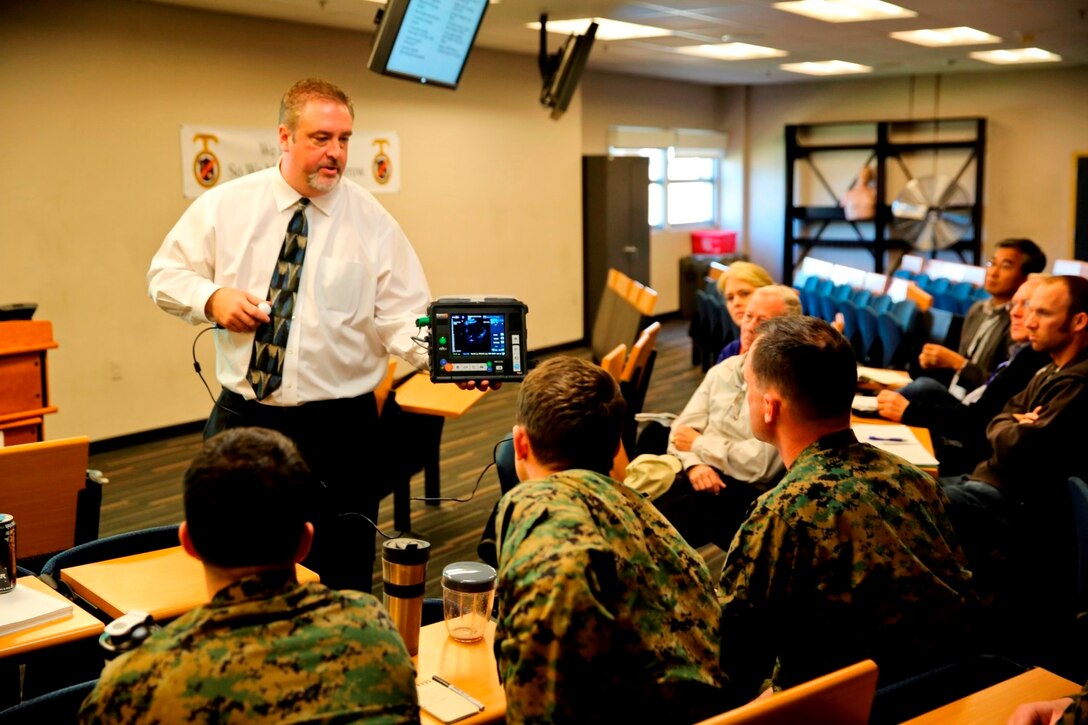 Marc Whedbe, director of U.S. military sales for Remote Diagnostic Technologies, from Virginia Beach, Va. talks to Marines and Sailors about the Tempus Pro, a tactical telemedicine device, over two days of informational and operational testing aboard Camp Pendleton, Calif., Jan. 22-23. The Tempus Pro attaches to the patient and broadcasts their vital signs back to a battalion aid station or aiding physician so that they can instruct and help the corpsman.